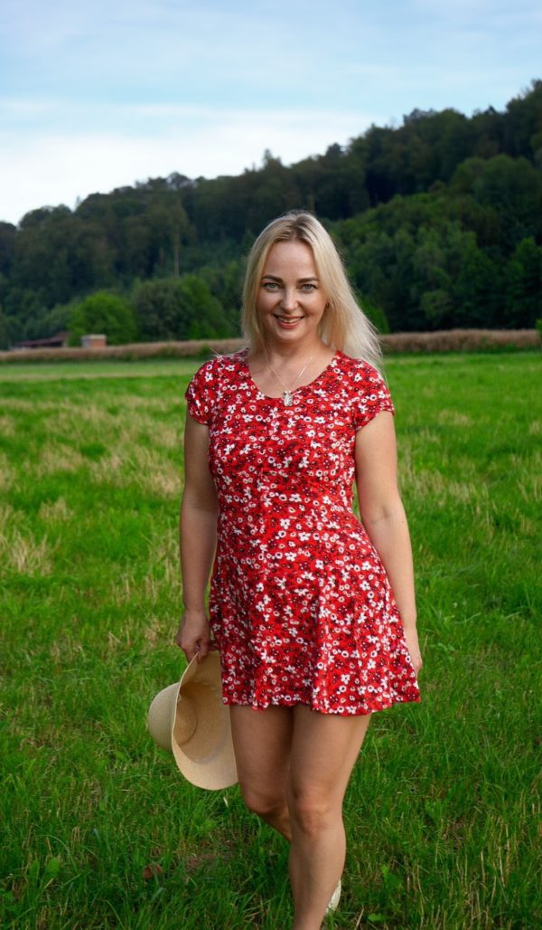 Polnische Single in Deutschland: Eine blonde Frau im roten Sommerkleid mit Hut genießt einen sonnigen Tag auf einer Wiese.