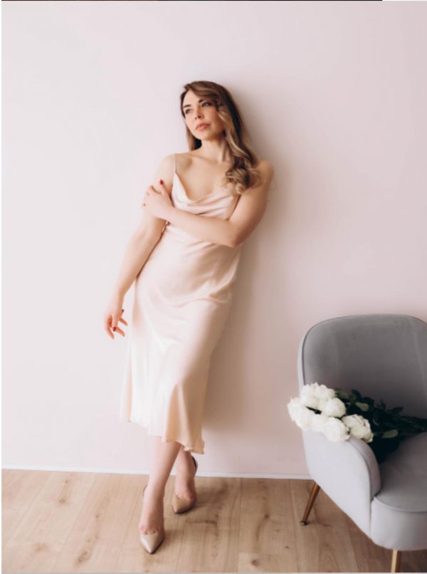 Antonina, 38 Jahre alt, posiert elegant in einem beigen Seidenkleid an einer hellen Wand. Auf einem Sessel neben ihr liegen weiße Rosen. Ausländische Single Frauen und Damen aus Osteuropa suchen eine Partnervermittlung, um ihr Glück zu finden.